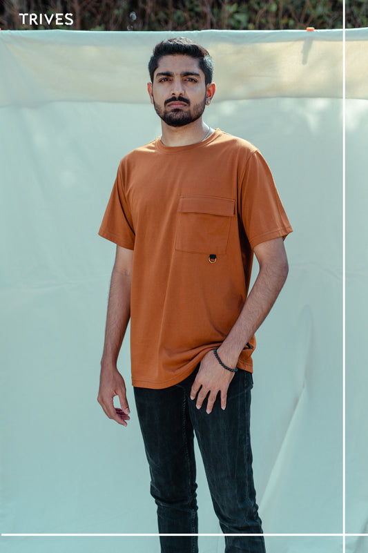 Man wearing a Trives Cocoa stash tee / t-shirt with a pocket and dark jeans against a light background