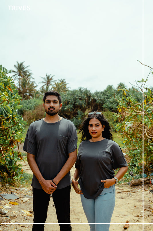 Two people standing in a natural setting with greenery around them. Trives Fray Tee couple tshirt wearing.