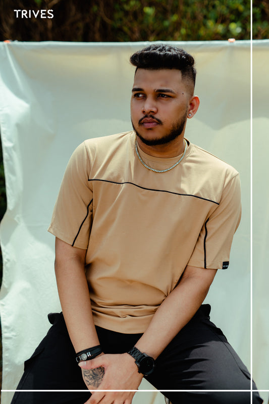 Man wearing a TIVES beige horizon t-shirt with black accents sitting against a white backdrop