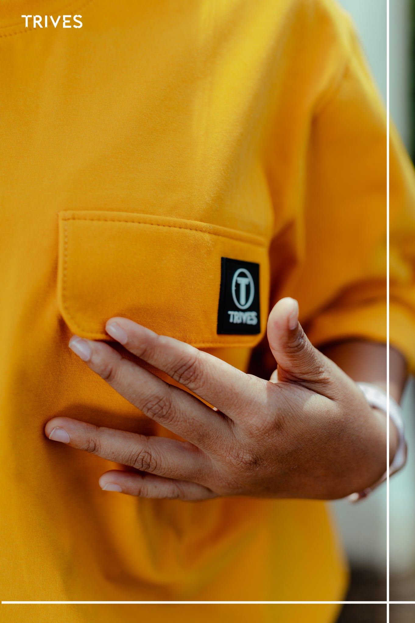 Yellow shirt with a visible brand logo on a blurred background. Trives Tee