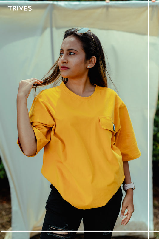 Woman wearing a yellow shirt with a visible brand logo, standing outdoors. Trives Vault Tee
