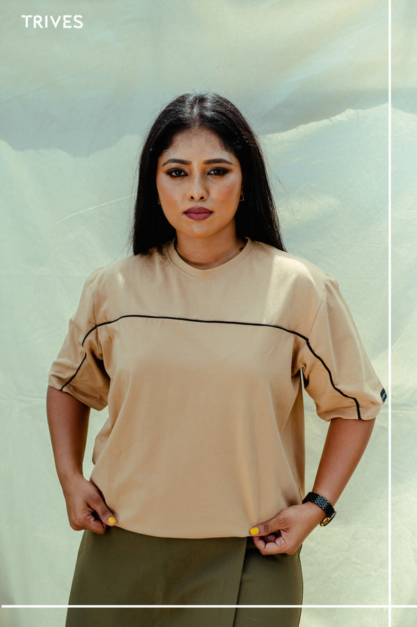 Woman wearing a TRIVES beige top with black trim against a light green background