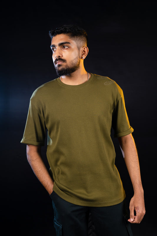 A person wearing a green crew neck trives t-shirt with an embroidered design on the shoulder