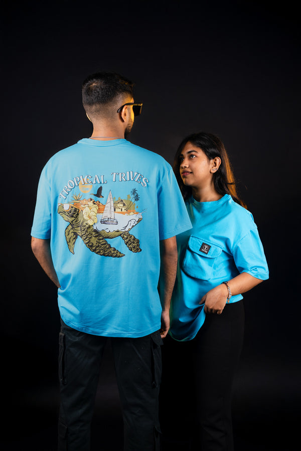 Two individuals are wearing blue unisex Trives T-shirts with a puff-printed design of a turtle on the back, on the front, the T-shirt has a 3D pocket.